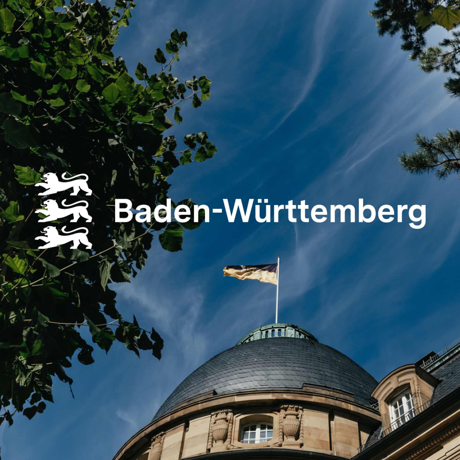 Logo von Baden-Württemberg vor Staatskanzlei mit wehender Flagge