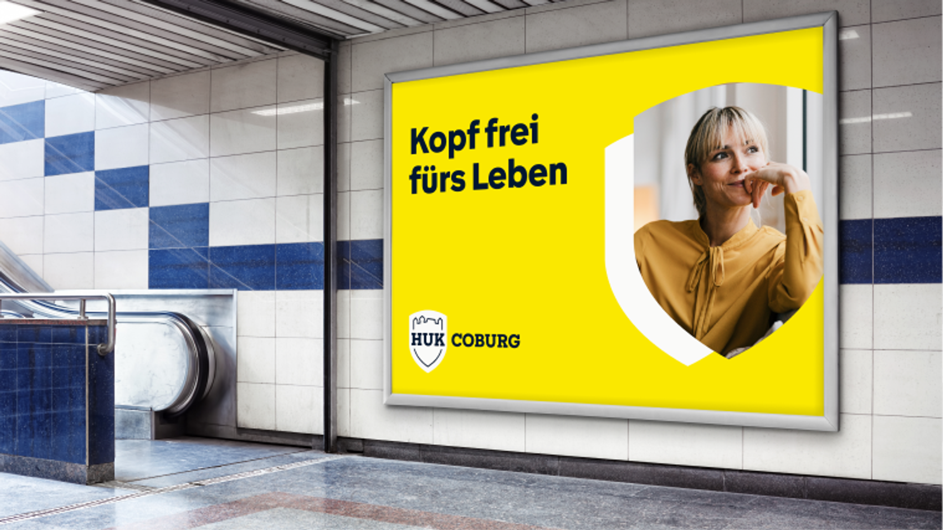 Ein großes U-Bahn Werbeplakat zeigt das Porträt einer lächelnden Frau in einer schildförmigen Aussparung und den Slogan „Kopf frei fürs Leben"