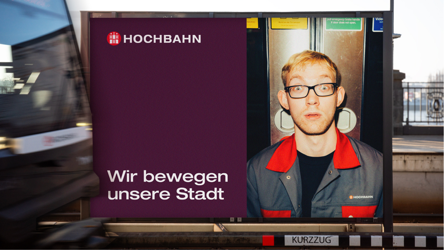 Hochbahn-Plakat: Mann in Arbeitskleidung vor Bahntür, Logo und Slogan „Wir bewegen unsere Stadt" auf Violett.