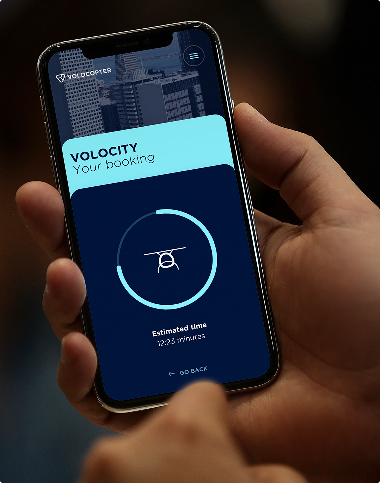 Volocopter App-Screen „Volocity – Your booking": Flugstatus-Ansicht mit Ladekreis und „Estimated time 12:23 minutes"