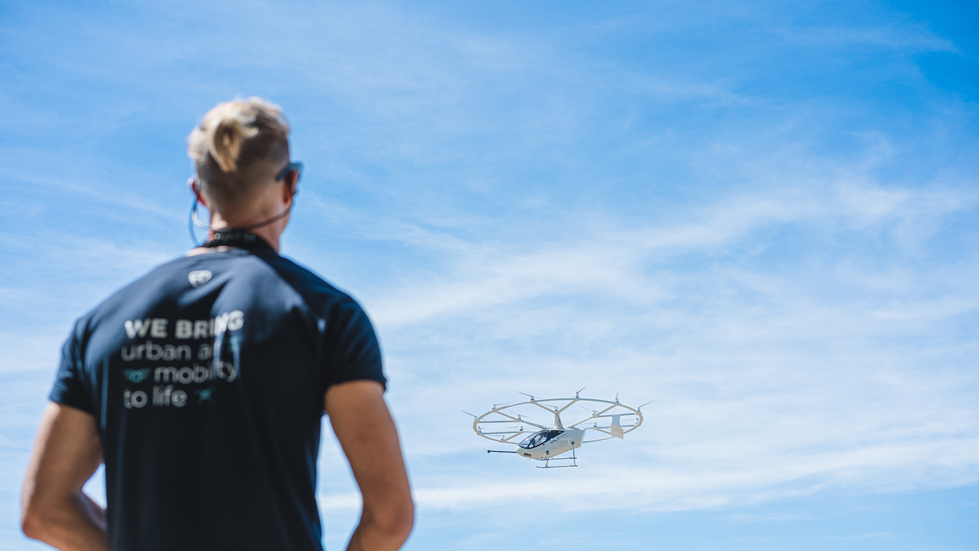Volocopter-Mitarbeiter von hinten mit T-Shirt „We bring urban air mobility to life" beobachtet Fluggefährt