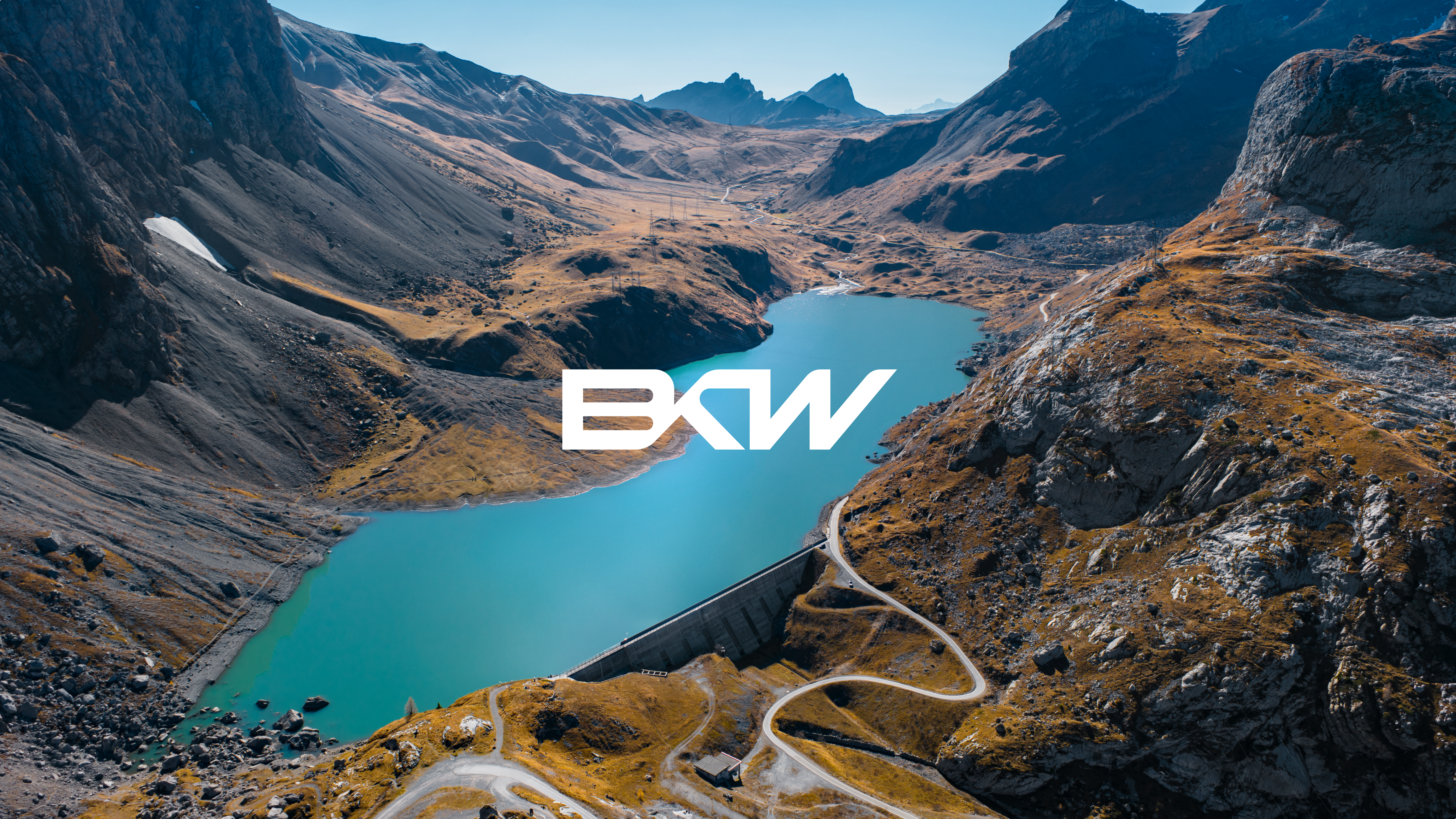 BKW Logo in Weiß vor einer Luftaufnahme einer Staumauer mit Stausee.