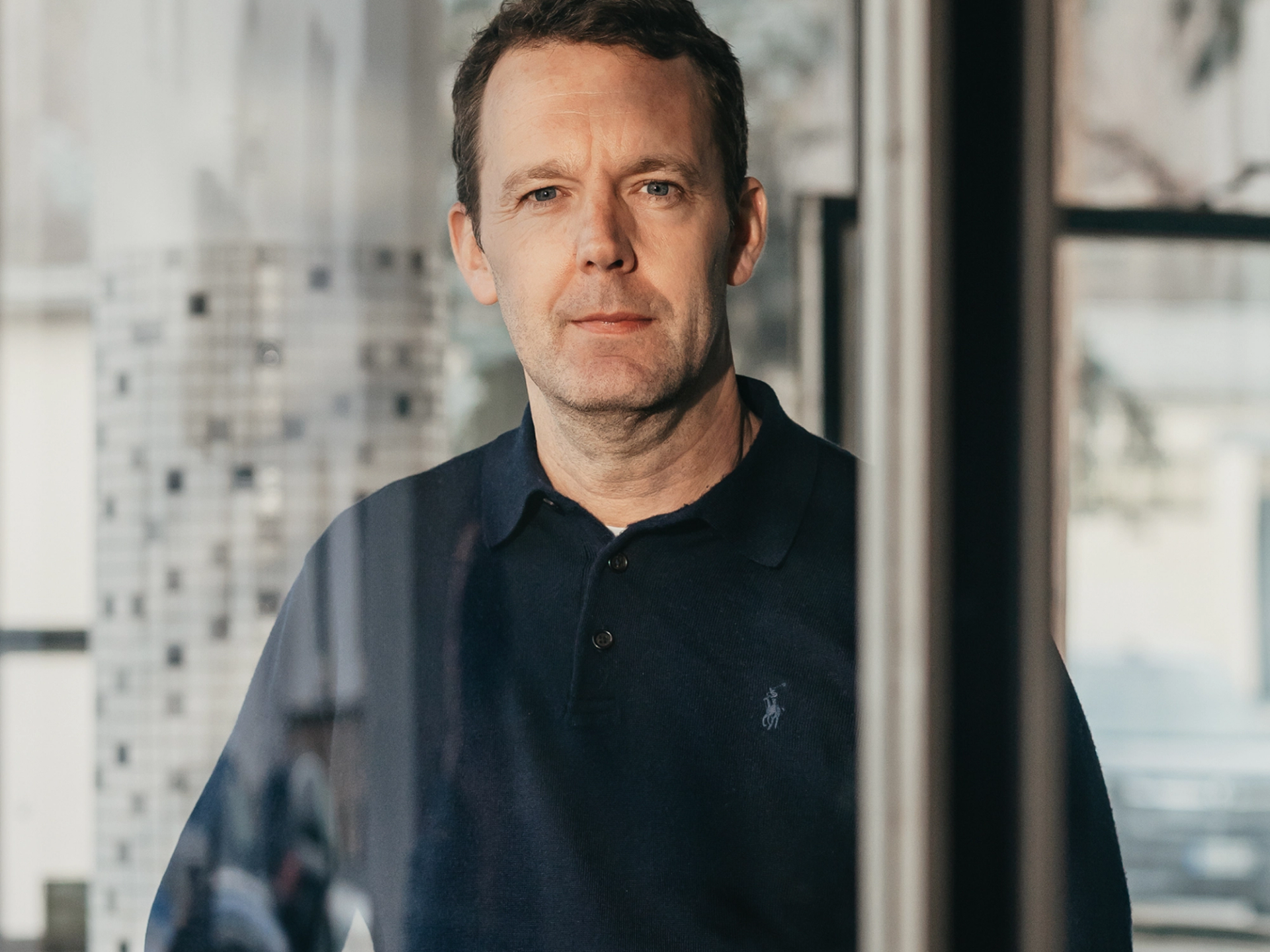 Porträtfoto von Philipp Brune im Polo-Shirt vor einer Fensterfront
