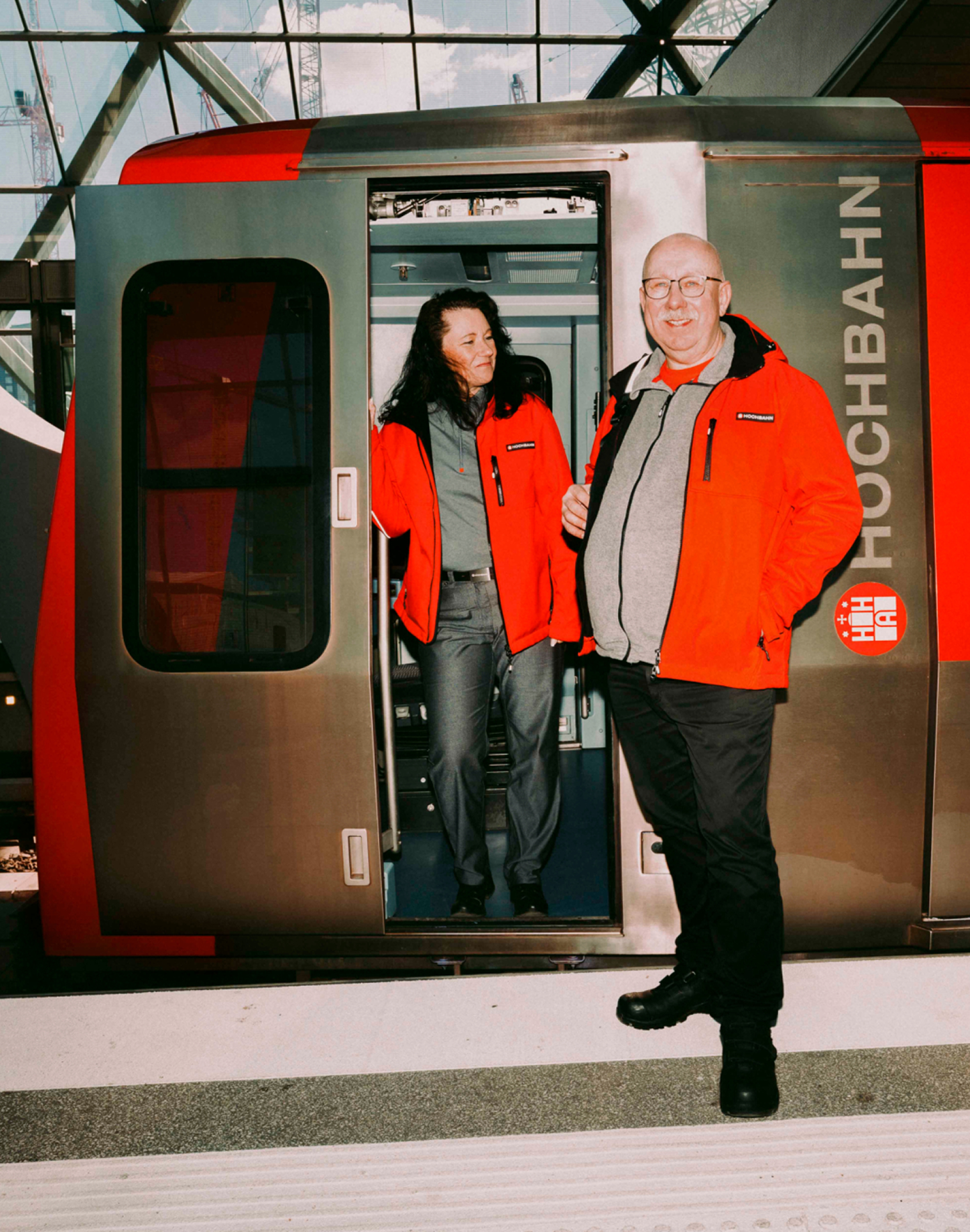 Zwei Mitarbeitende der Hochbahn in roter Arbeitskleidung vor einer U-Bahn.