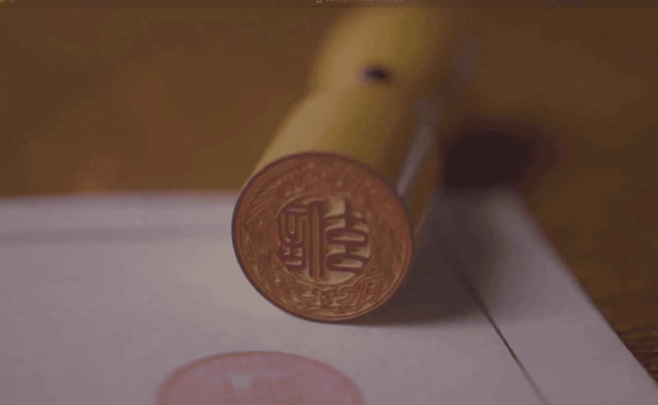 A pale hand-carved seal standing on white paper, its face cut with a circular character design, a faint red impression beside it.