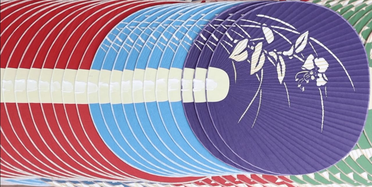 A stack of round flat fans in red, pale blue and purple, the top one printed with white leaves and flowers over its fine radiating ribs.
