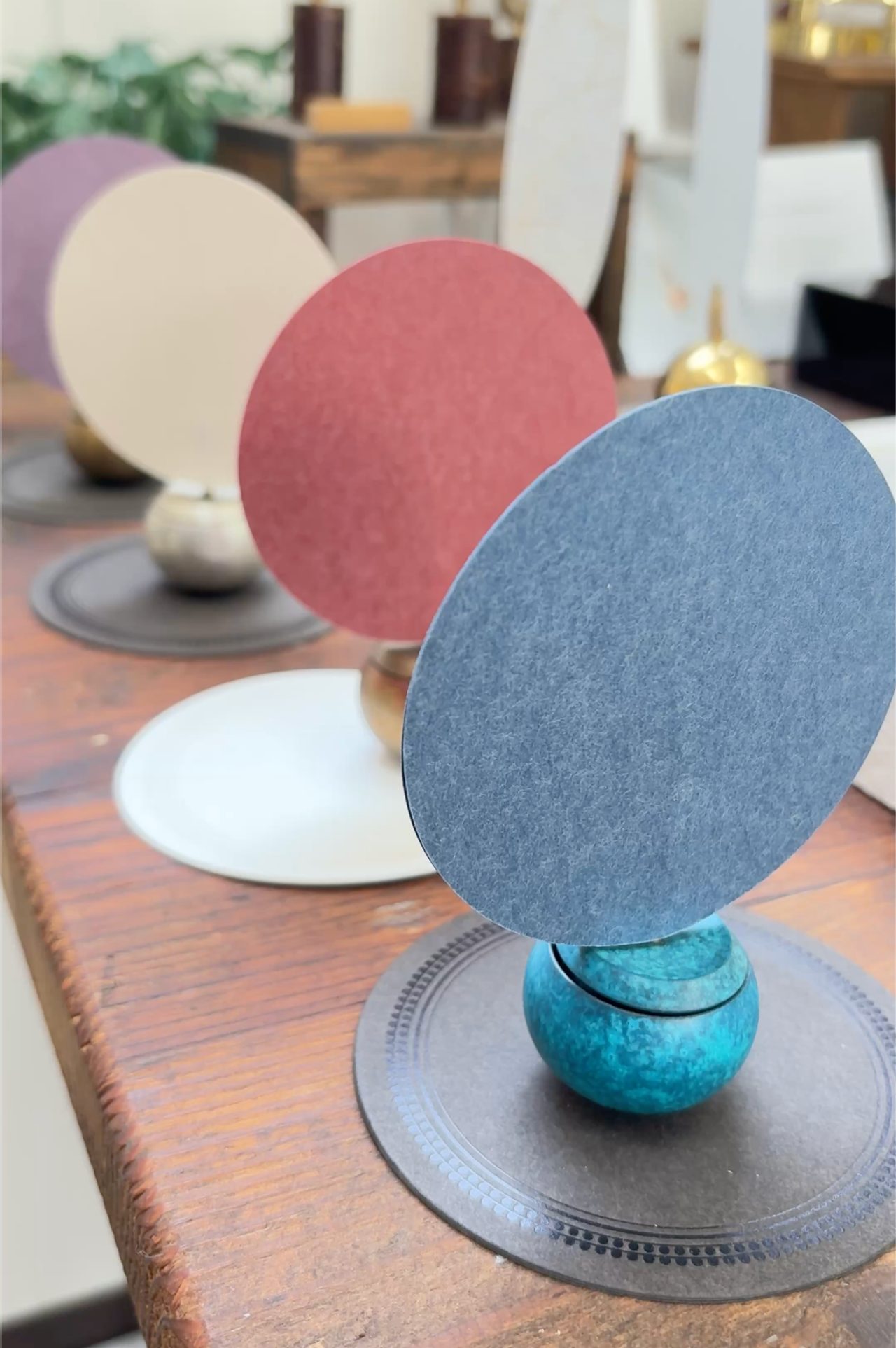 Round coloured discs standing upright on small glazed bases, arranged along a wooden bench.