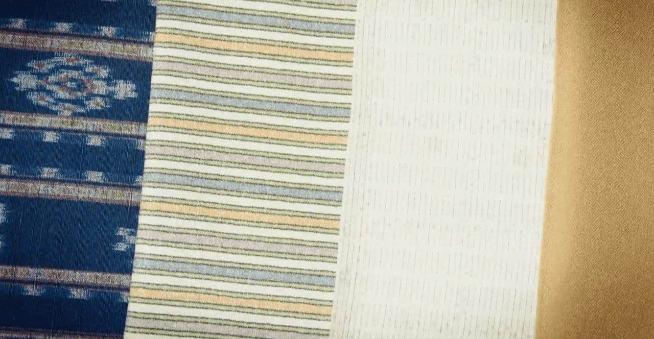Four lengths of woven cloth laid side by side, one indigo with white ikat medallions, one finely striped, one cream, one plain ochre.