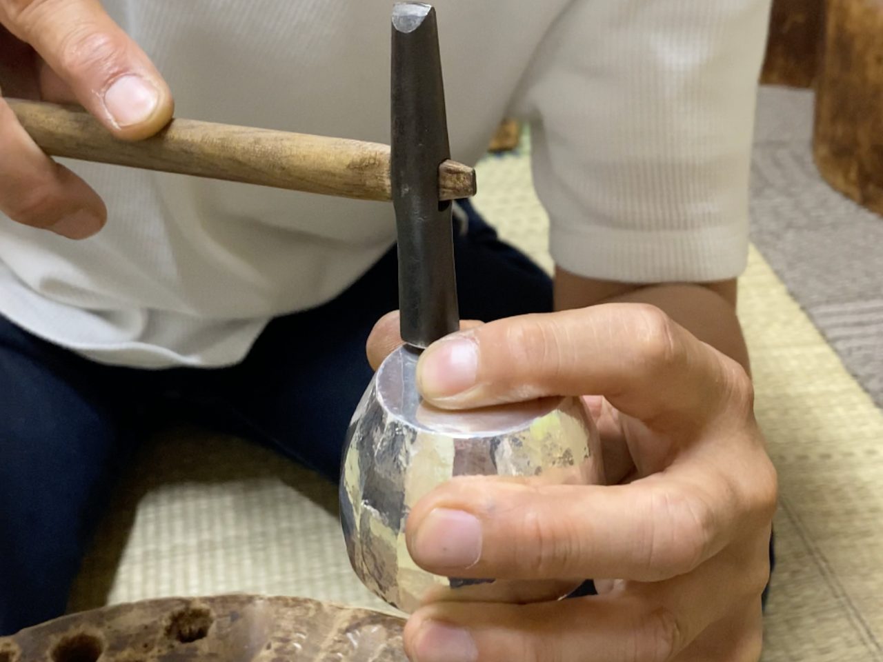 A person's hands with a hammer pounding on a silver craft 