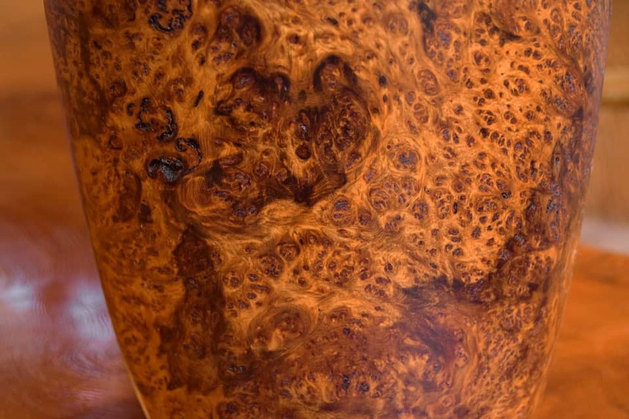 A close view of a turned cedar vessel, its surface a dense burl figure of swirling amber, ochre and dark brown grain.