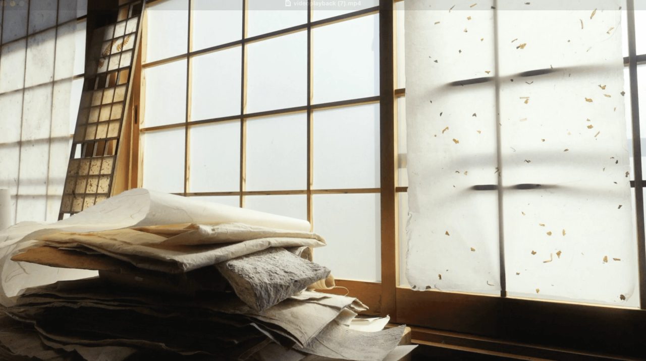 A stack of handmade paper sheets on a bench beside tall paper screens, with flecks of fiber visible in the backlit panel on the right.
