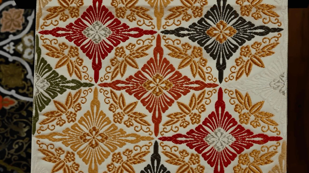 A panel of woven silk in cream, patterned with large diamond medallions of stylized leaves in gold, red, green and black.