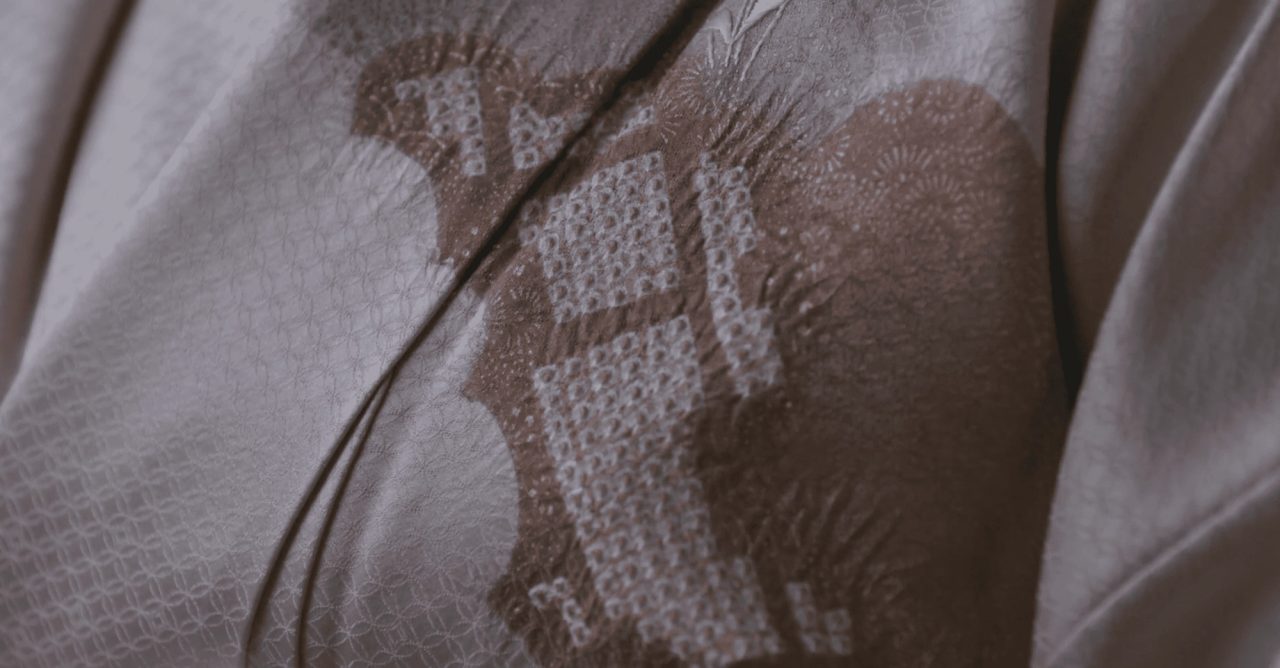 Close view of pale silk tie-dyed in fine puckered dots, forming a soft brown fan and floral motif across the folds.