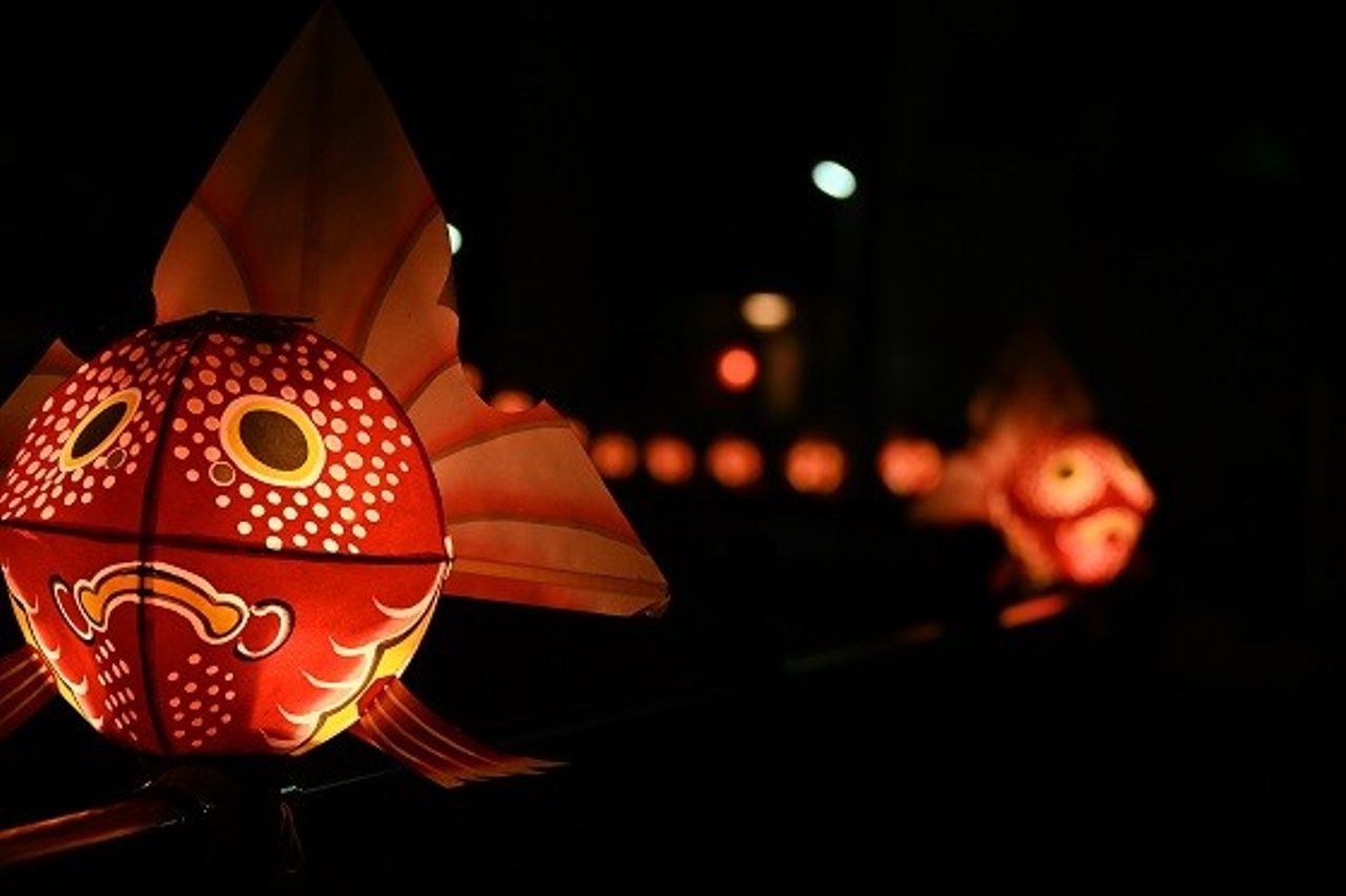 A round paper lantern painted as a red goldfish, lit from within at night, with more of them receding out of focus behind it.