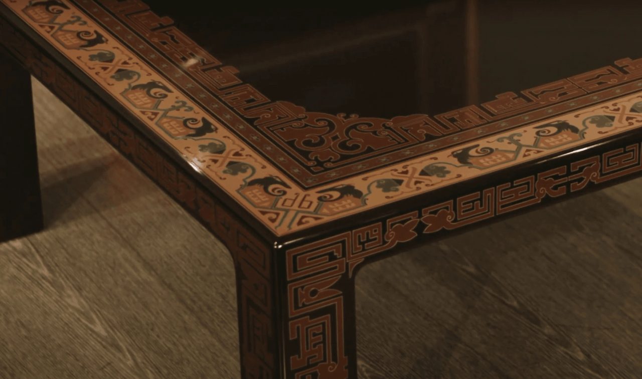 The corner of a low lacquered table, its black surface carved and inlaid with dense russet key-fret and animal patterns along every edge.