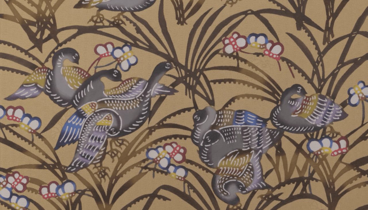 Cloth dyed with grey and blue birds among brown grasses and small red and white blossoms on a warm ochre ground.