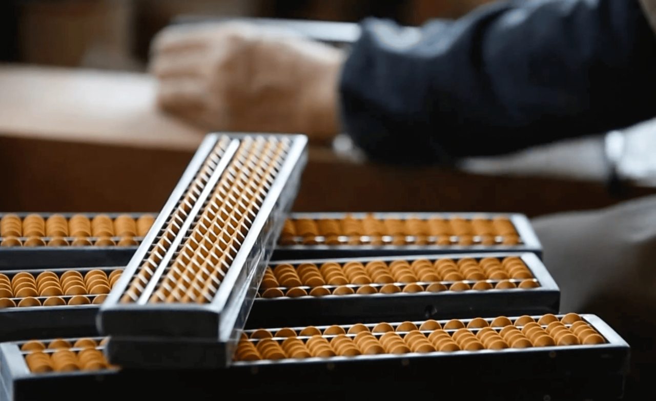 Several abacus frames stacked on a bench, their wooden beads threaded on rods, with a partly assembled frame laid across the top.