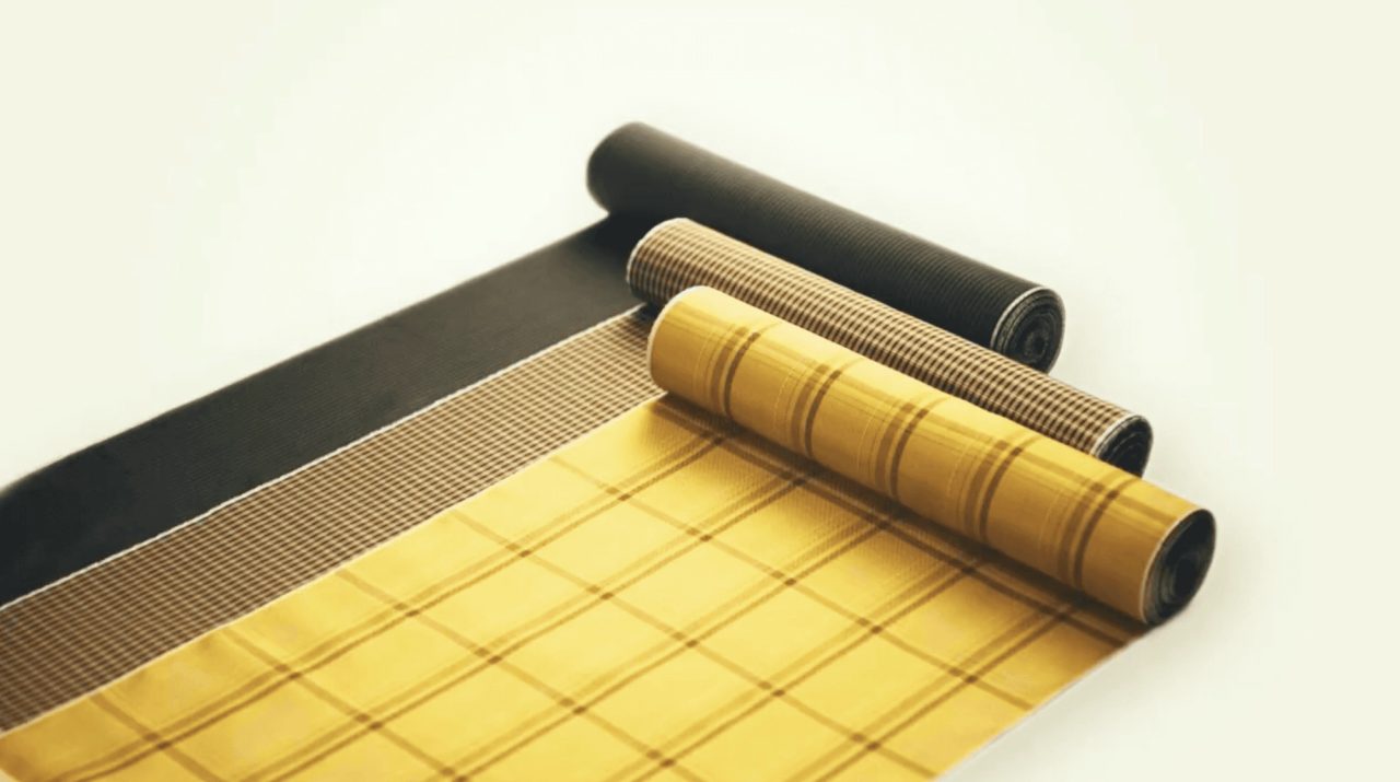 Four bolts of silk part-unrolled on a pale surface, in black, fine brown check, yellow stripe and yellow with a dark grid.