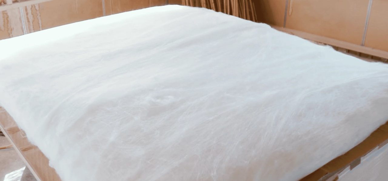 A wide sheet of stretched silk floss laid over a wooden frame, translucent white with the fibers running in soft layers.