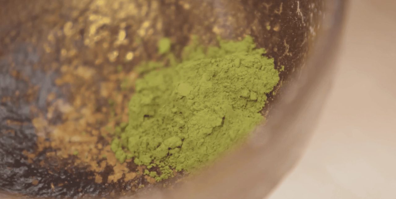 Bright green tea powder mounded in the base of a dark stone grinding bowl, seen close and from above.