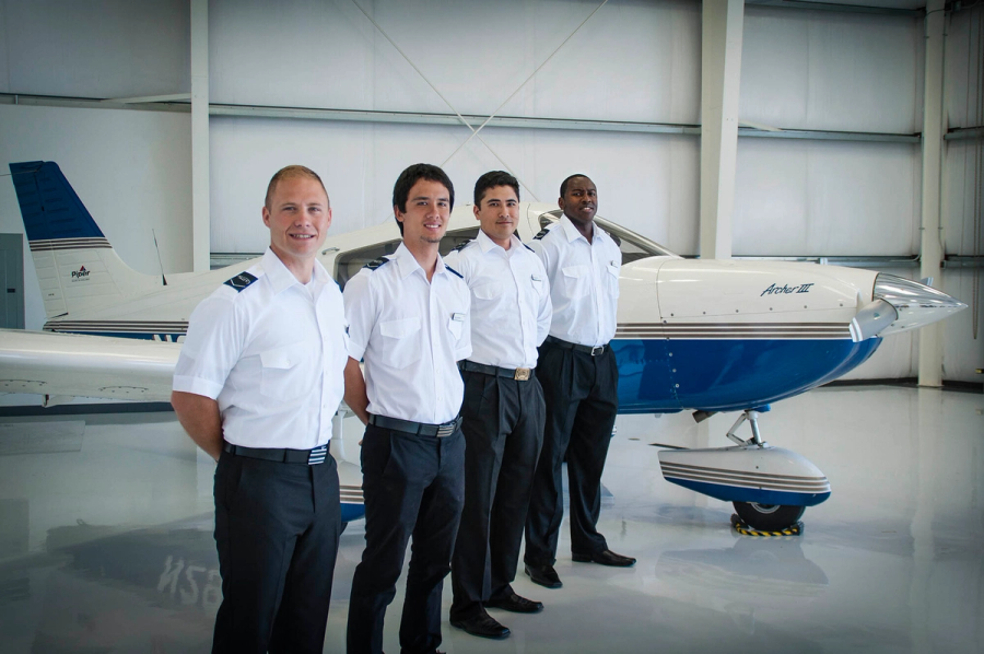 Four Coast students in uniform beside a Piper Archer in the hangar