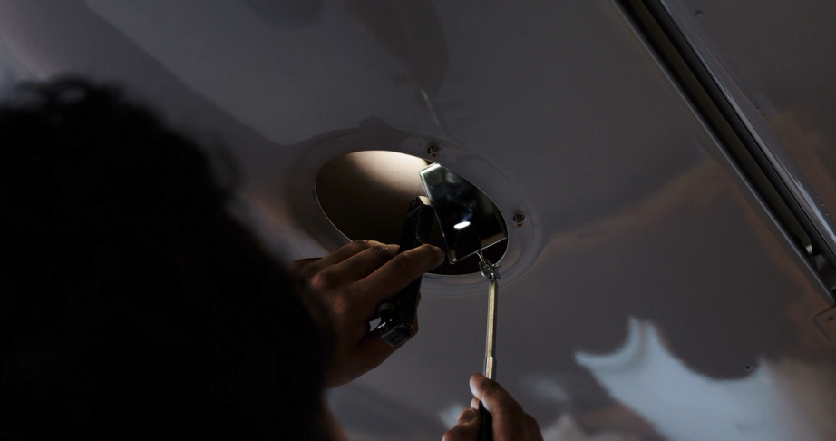 Coast mechanic inspecting an access panel with a mirror and torch