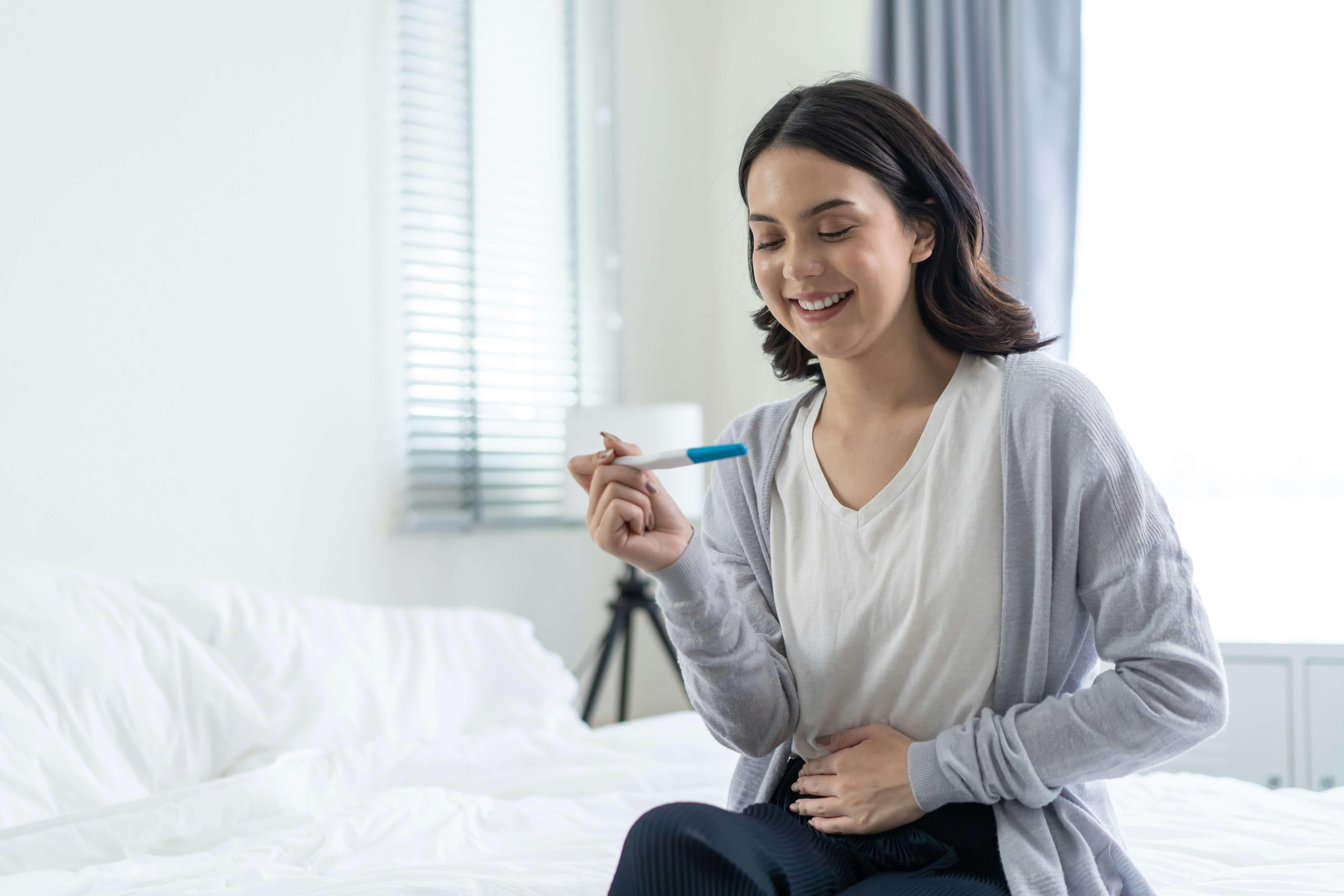 Woman reading a health test result on a bed holding her stomach