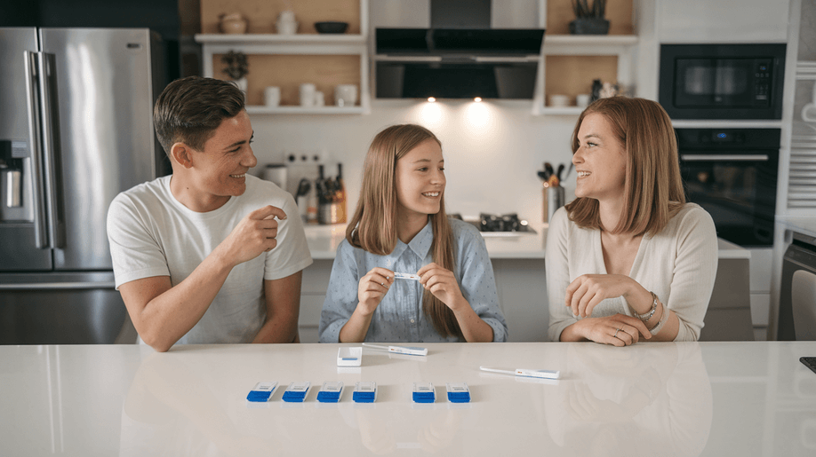 A mother and two children in a modern kitchen use rapid health self-test kits