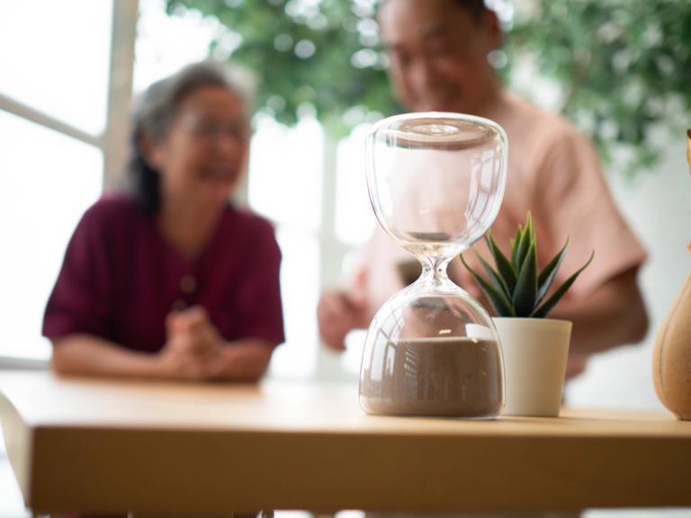 Hourglass on a table symbolizing the passage of time, with two people blurred in the background, symbolising the concept of drug detection duration for cannabis and cocaine
