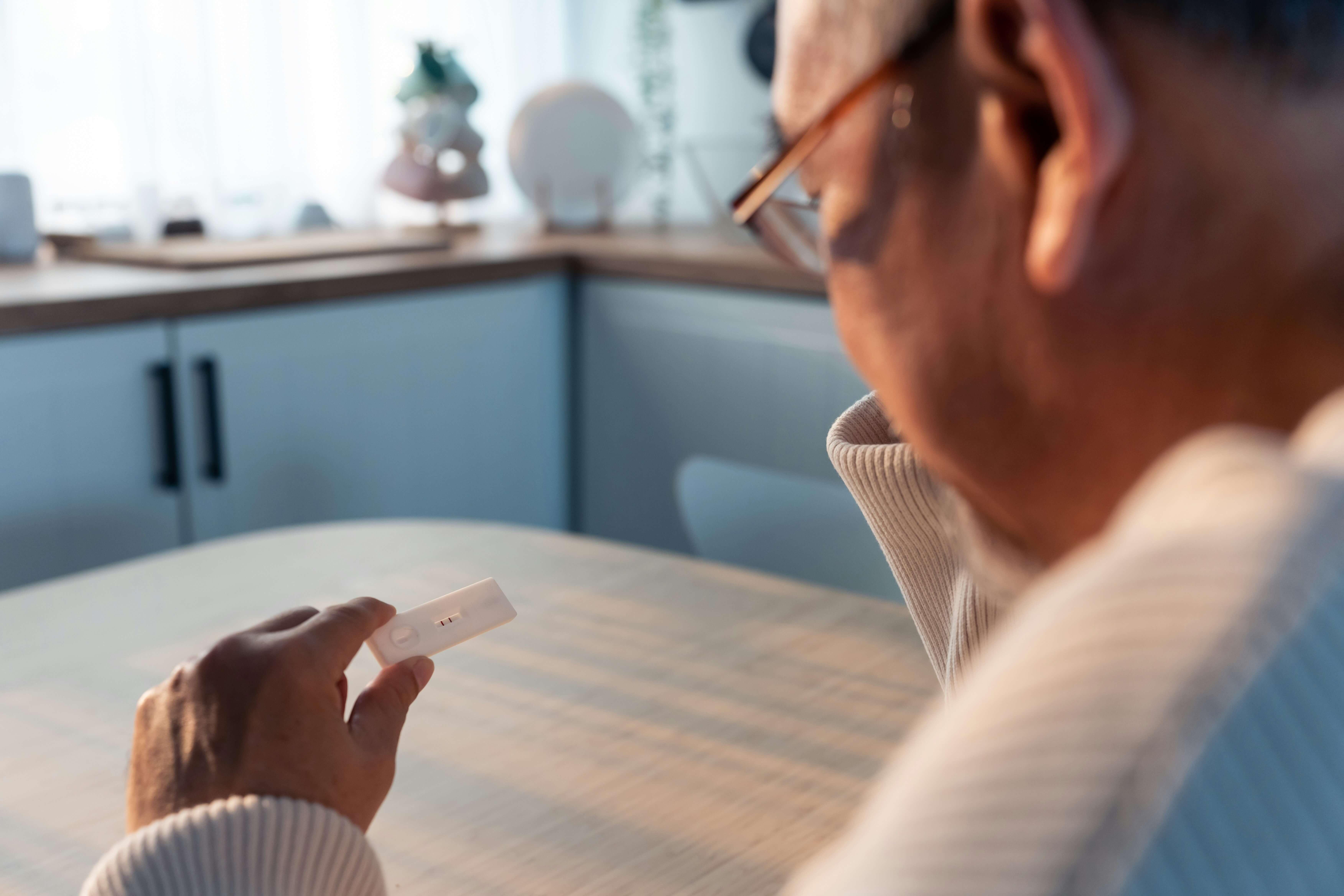 Older man reading a rapid health test sitting at a kitchen table