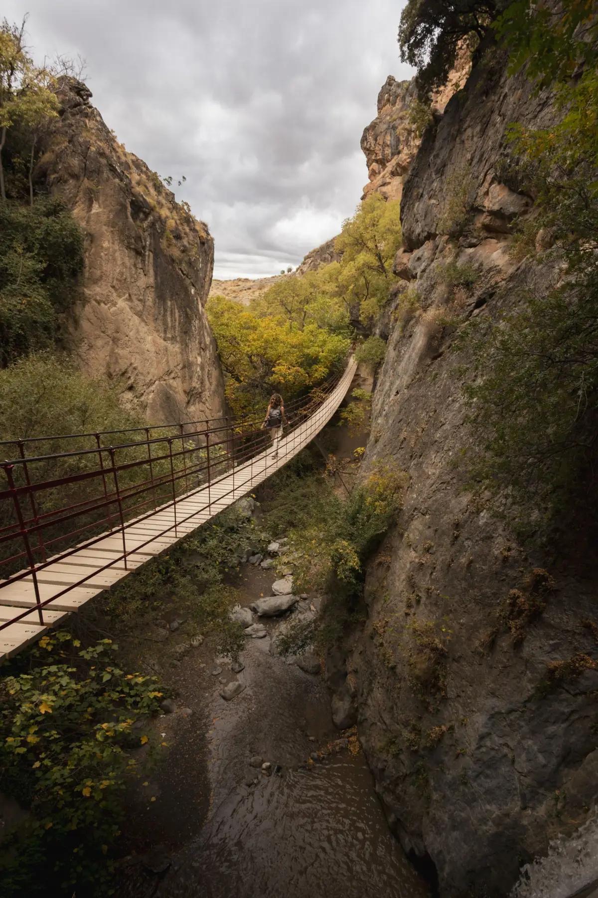 Walker crossing a hanging footbridge over the Monachil river in the Los Cahorros de Monachil gorge