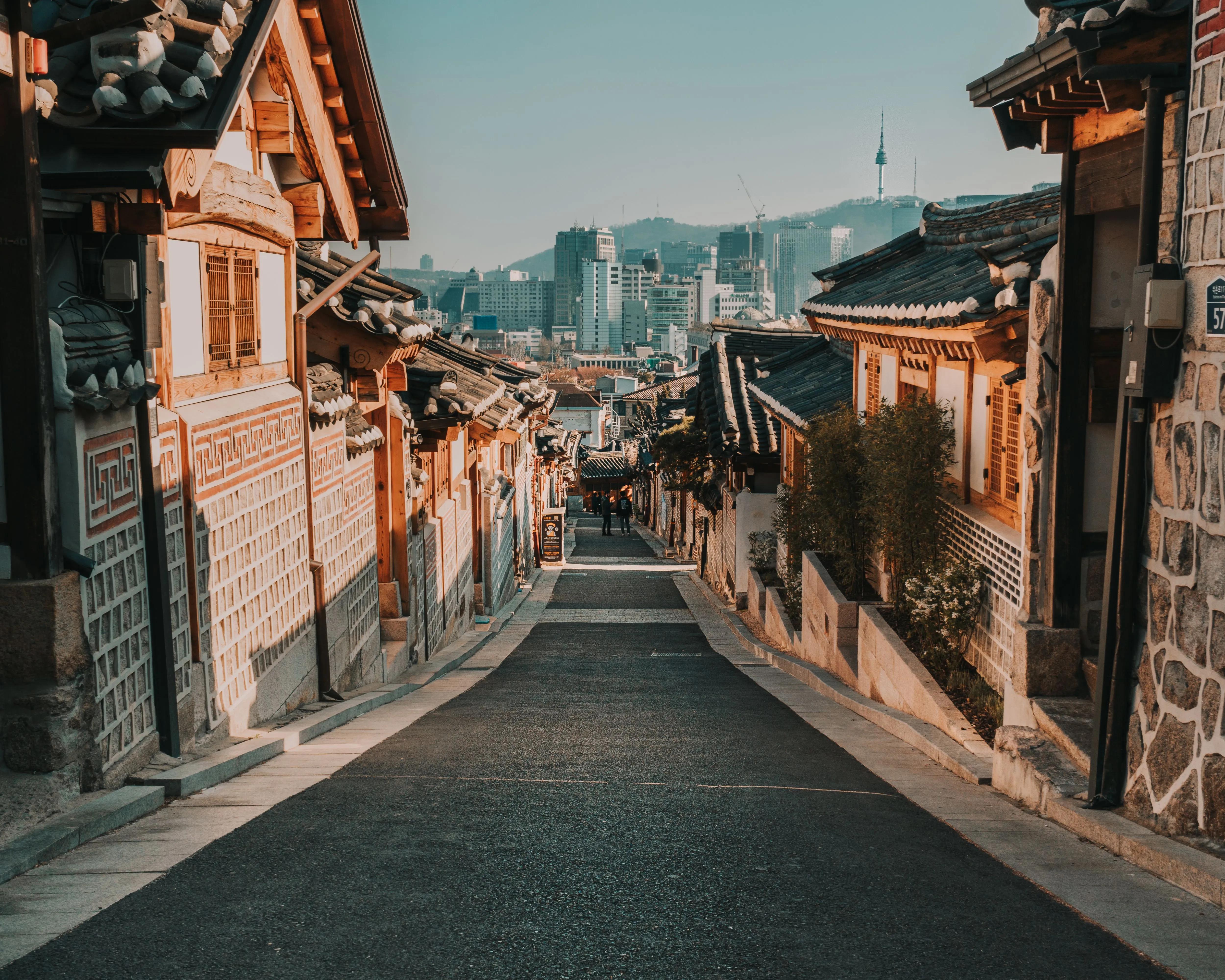 Quiet street between traditional hanok houses in Bukchon with N Seoul Tower visible on the hillside beyond
