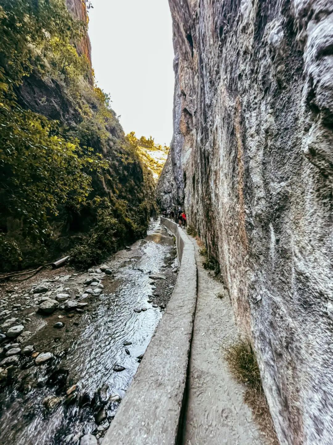 Hikers on the narrow path beside a water channel in the Los Cahorros de Monachil gorge, a popular spot for hiking near Granada