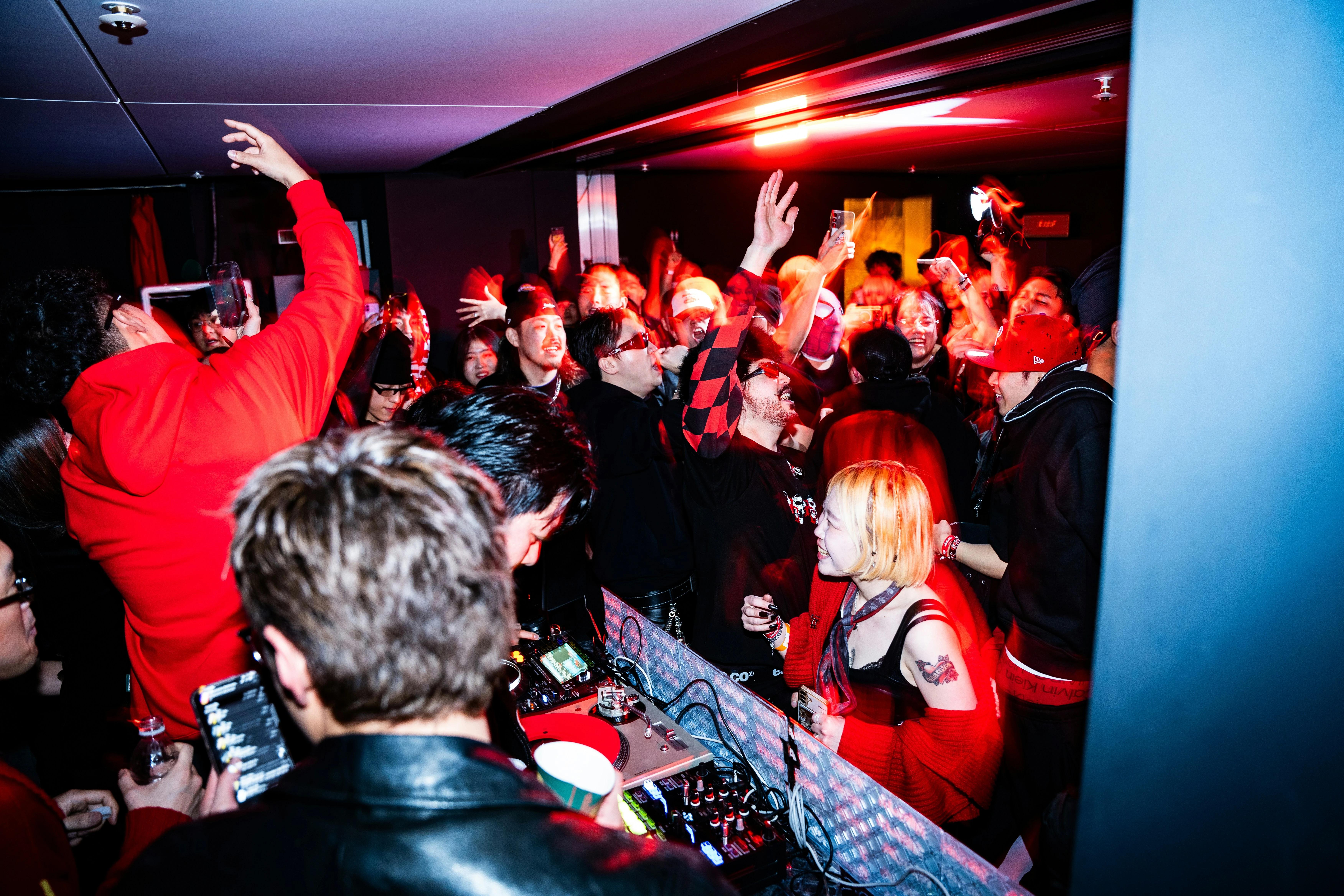 Busy nightlife spot in Hongdae with DJ decks in the foreground and crowd dancing under red lighting