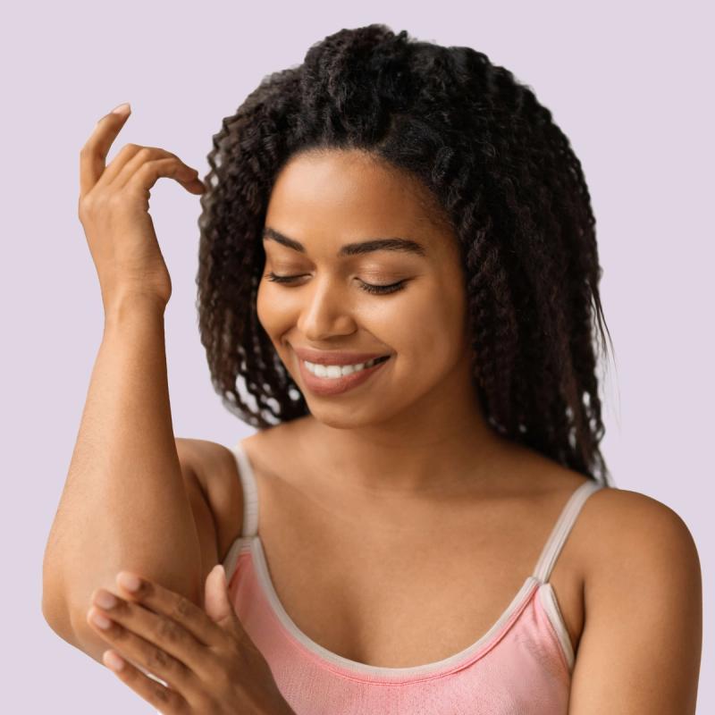 Woman looking at healthy skin on her arm and smiling.