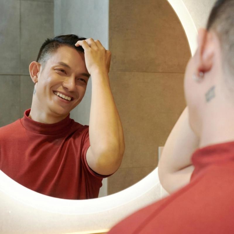 Man running his fingers through his hair and smiling into a mirror.