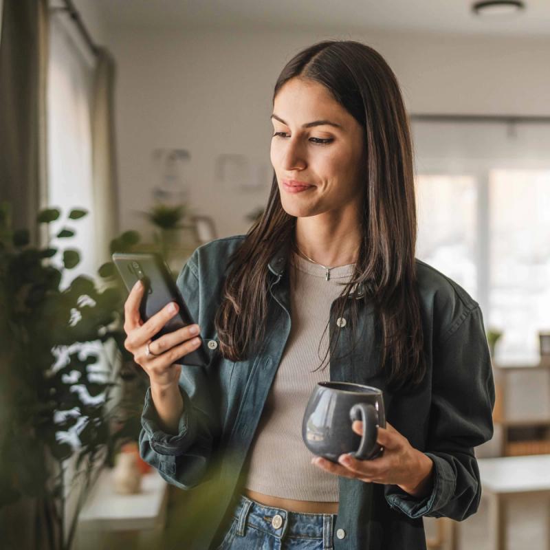 Confident woman looking at her phone and holding a coffee mug.
