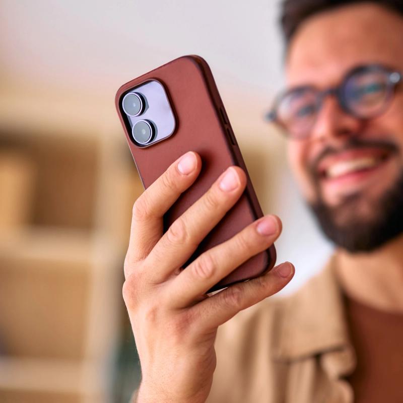 Bearded man in glasses holding a phone in a brown leather case.