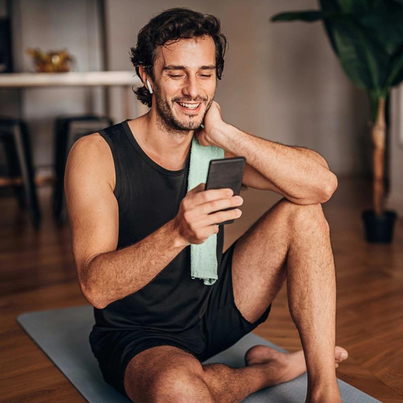 Man sitting on a yoga mat looking at his phone