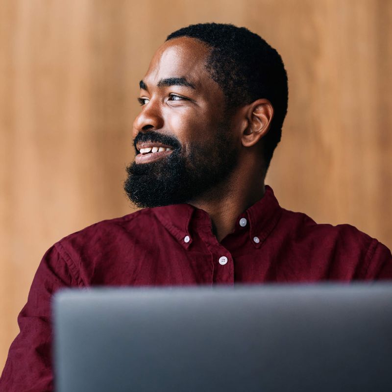 Man sitting behind laptop smiling off to the distance