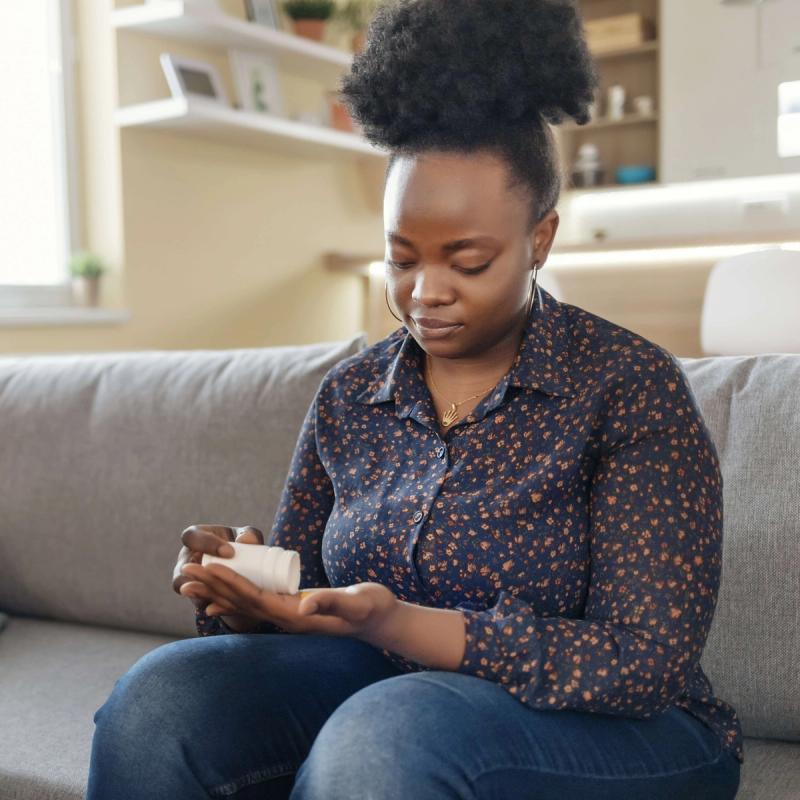 Woman Sitting on Couch Looking at Pill Bottle