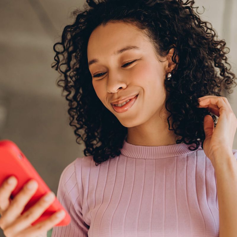 Woman smiling at phone with hand running through her curly hair.
