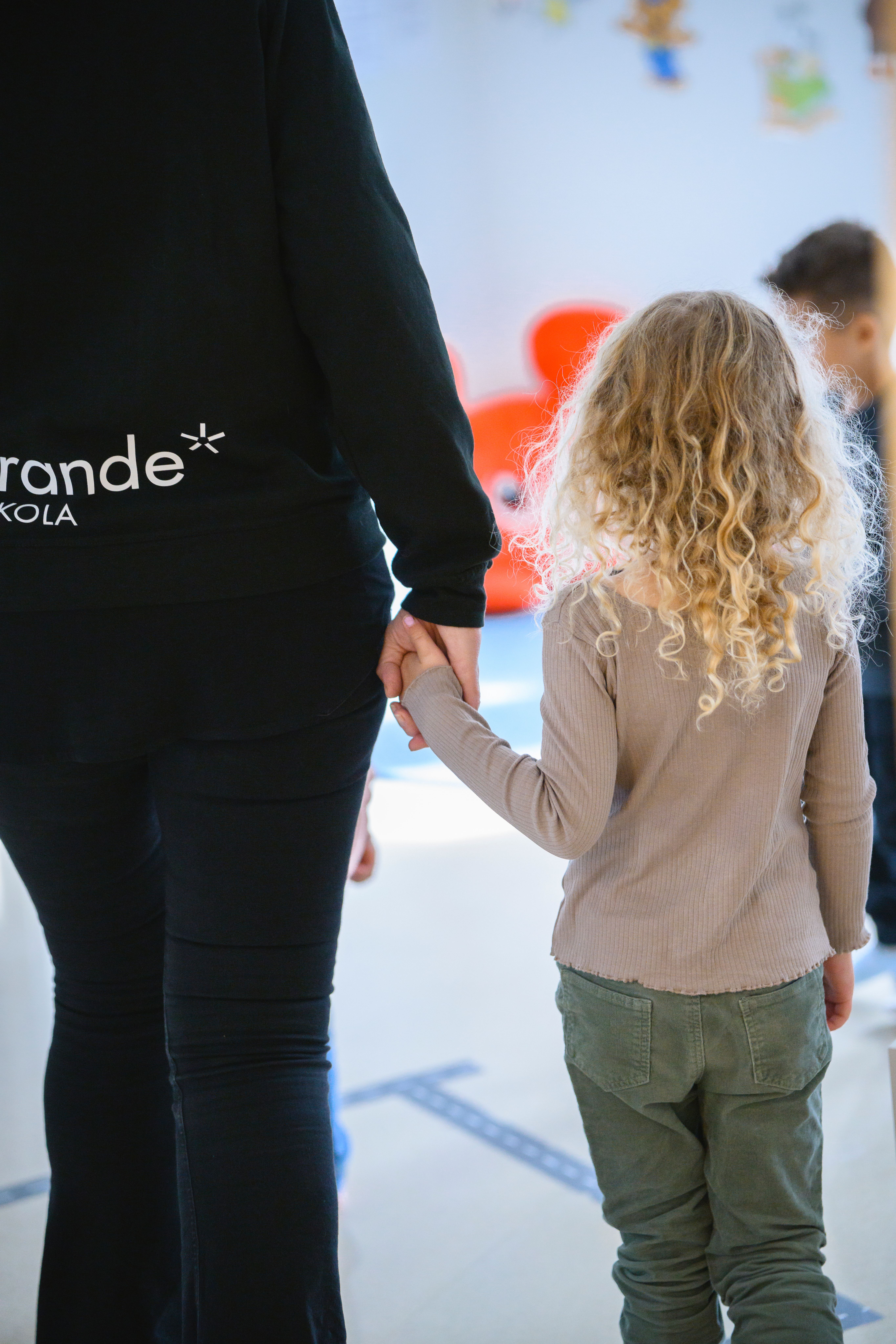 pedagog och barn, vända med ryggarna mot oss, som håller varandra i handen