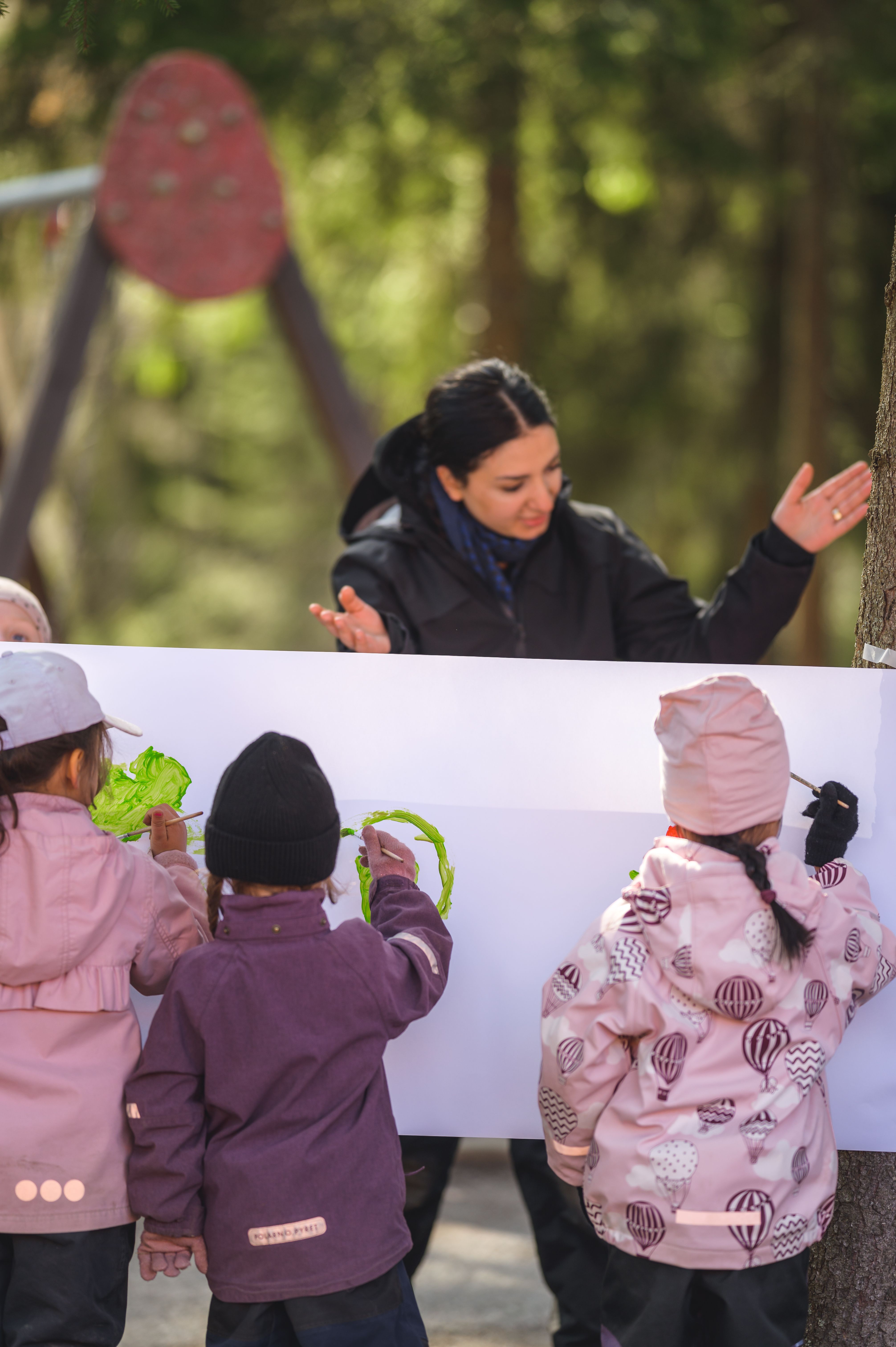 pedagog utomhus med tre barn som målar på staffli
