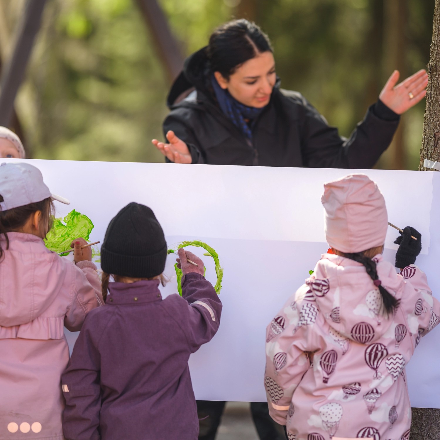 pedagog utomhus med tre barn som målar på staffli