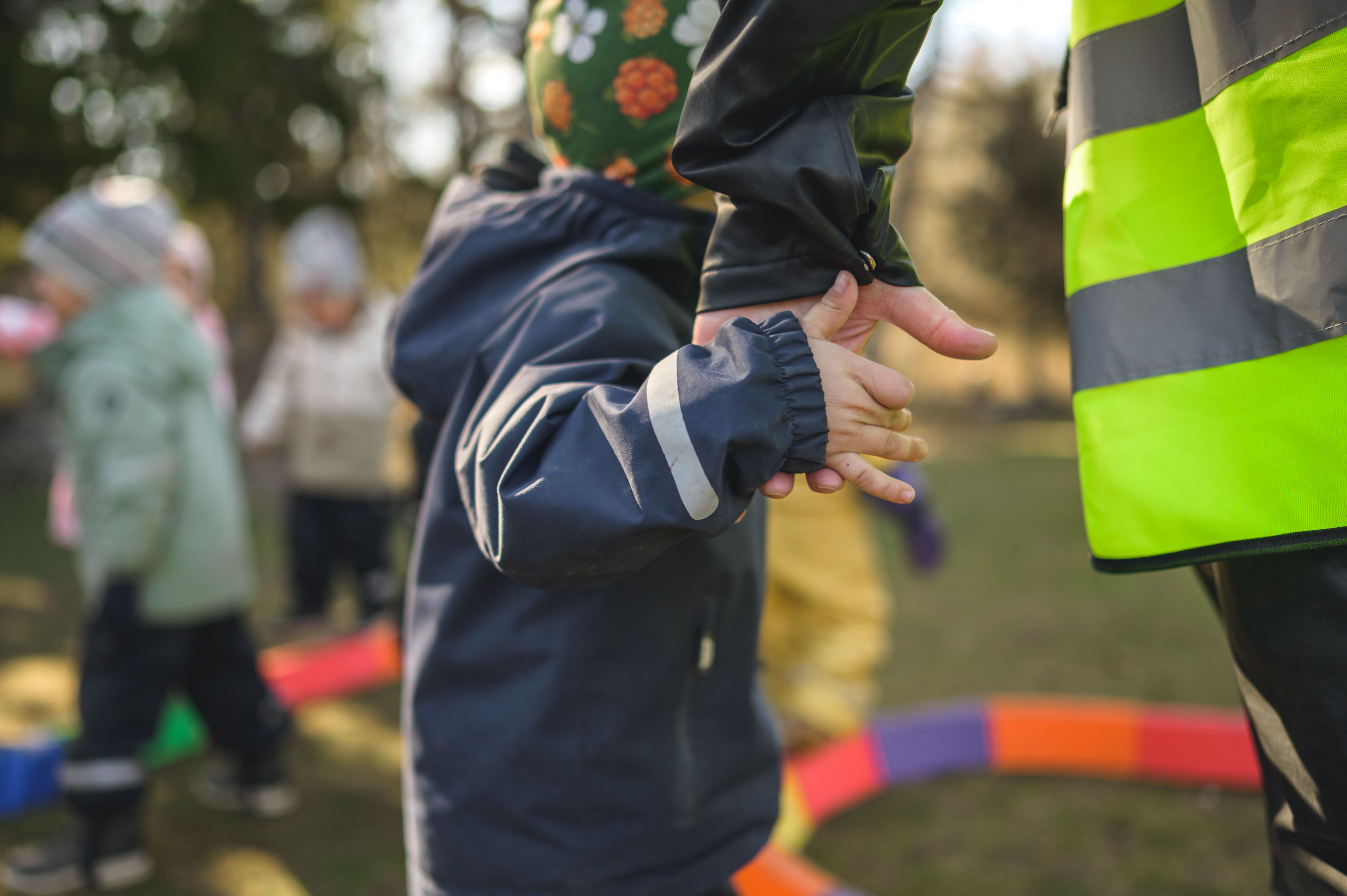 Barn håller pedagog i handen utomshus