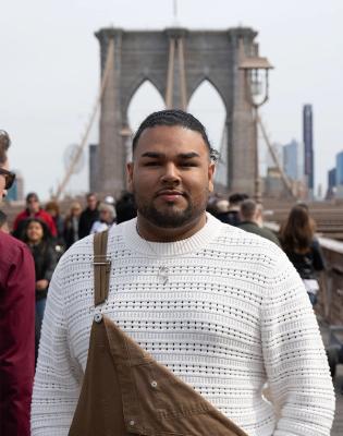 Photo of Marlon Castillo wearing a brown overall over a beige sweater, smiling kindly at the camera.