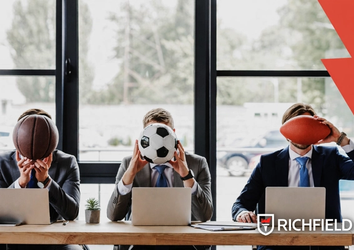 Men siting at a desk in an office setting with football, basketball and rugby balls. Richfield logo in bottom left corner.