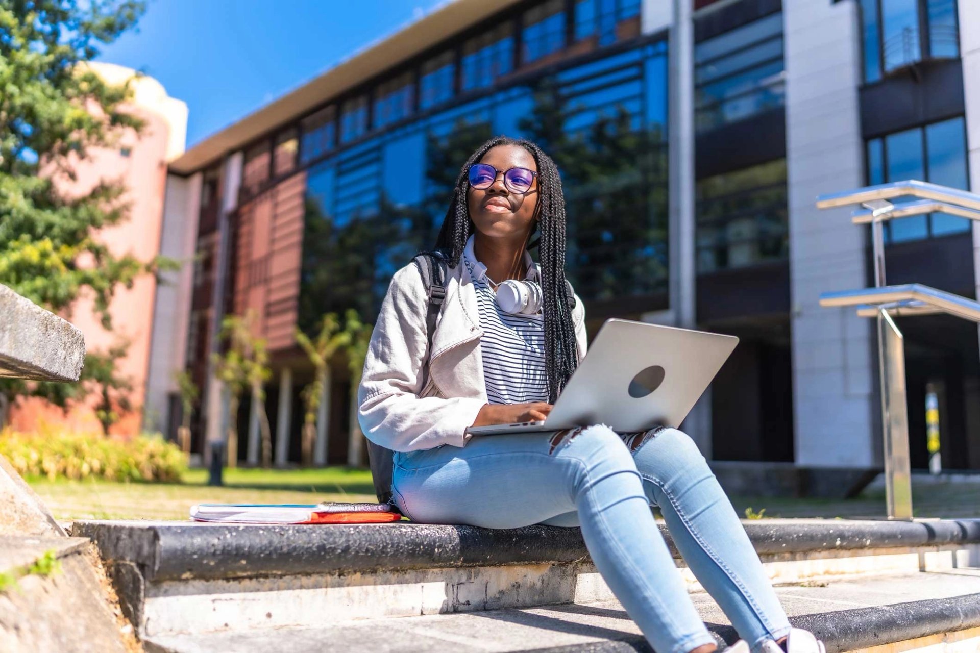 student sitting outside campus building with laptop