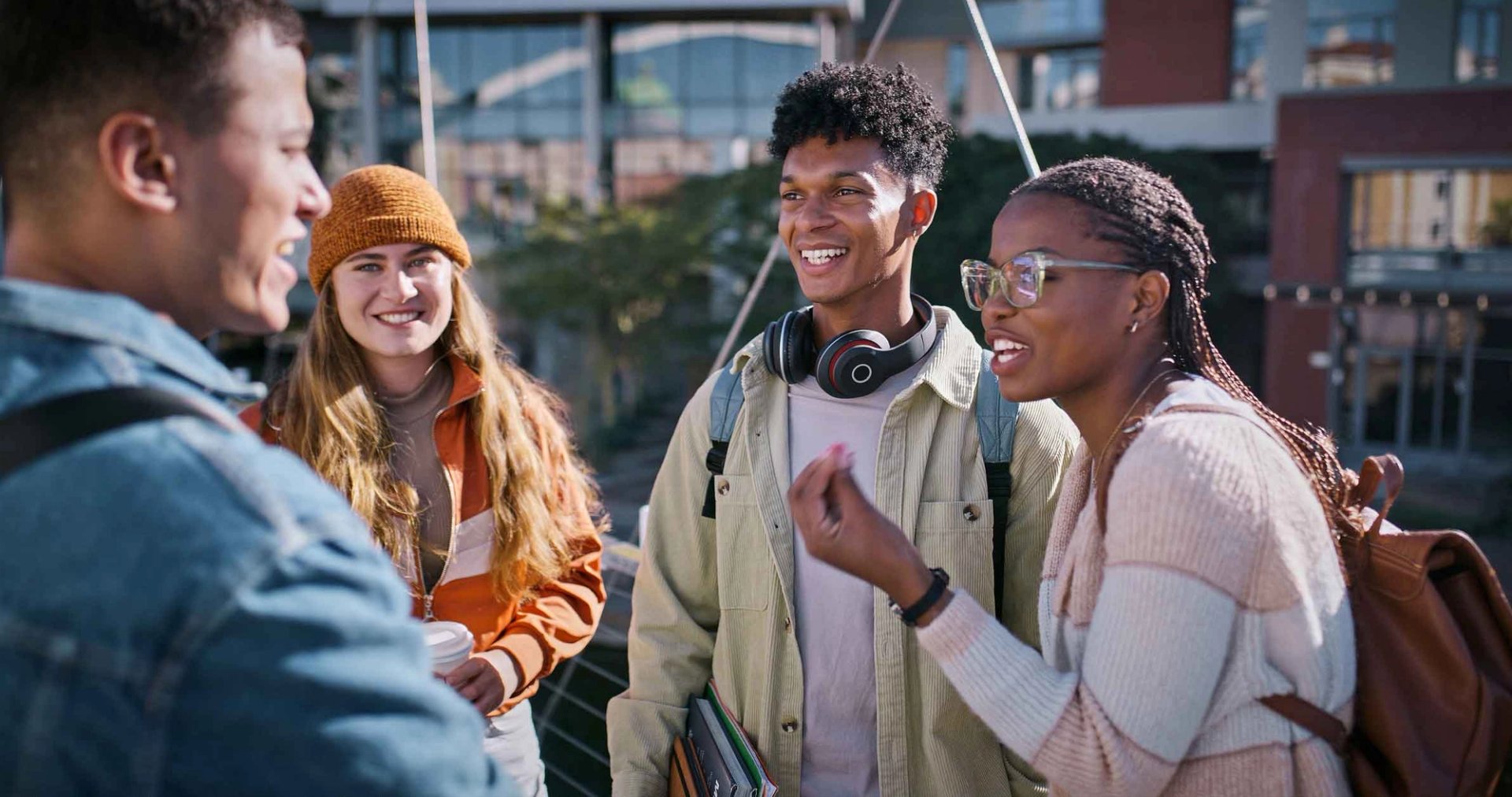 Two students walk past residence halls, talking and carrying binders.